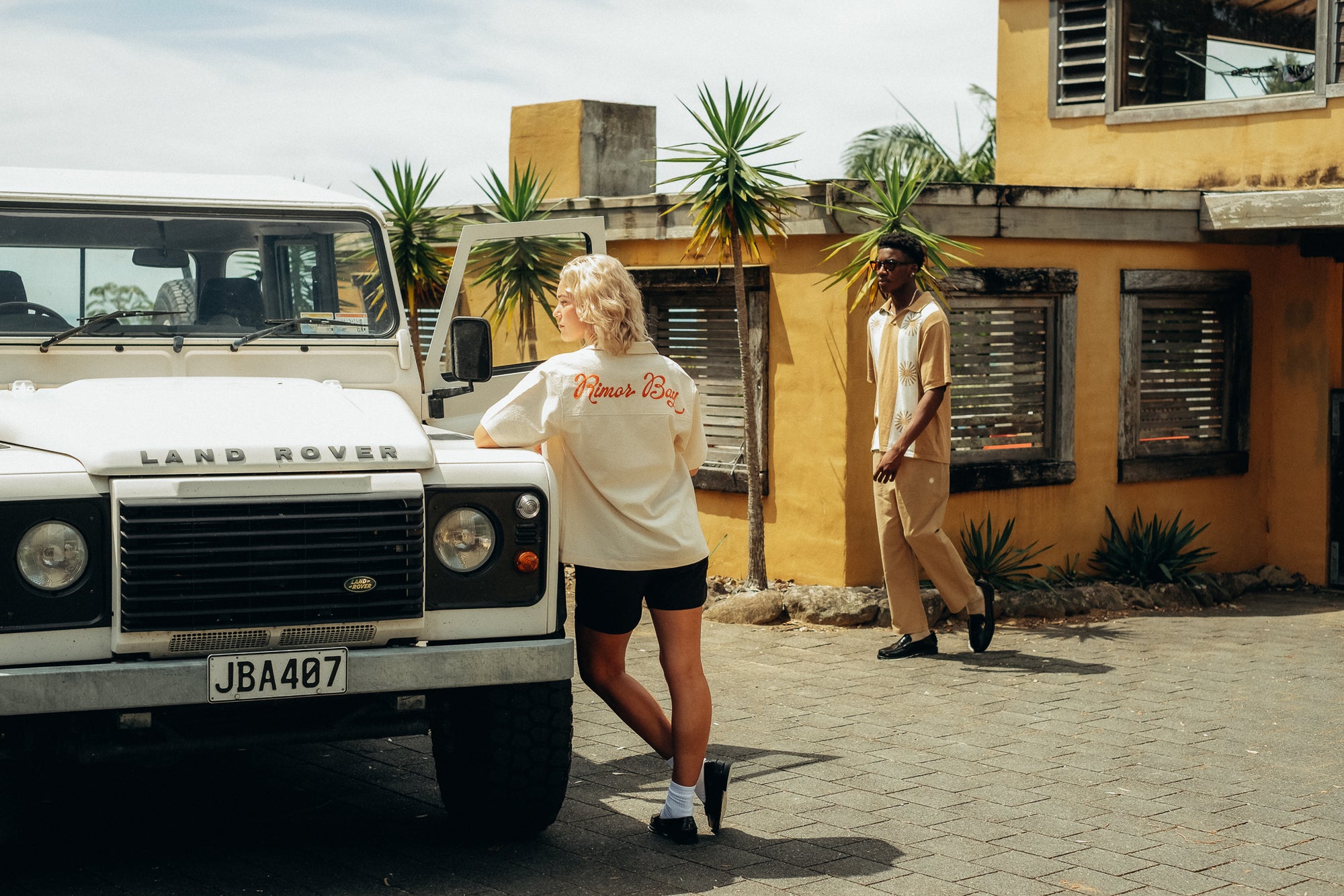 Woman leaning against white Land Rover, male walking towards her