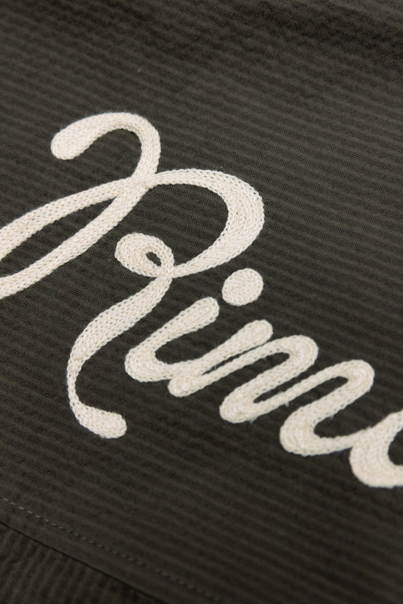 detail close up of khaki and beige cursive chain stitch logo