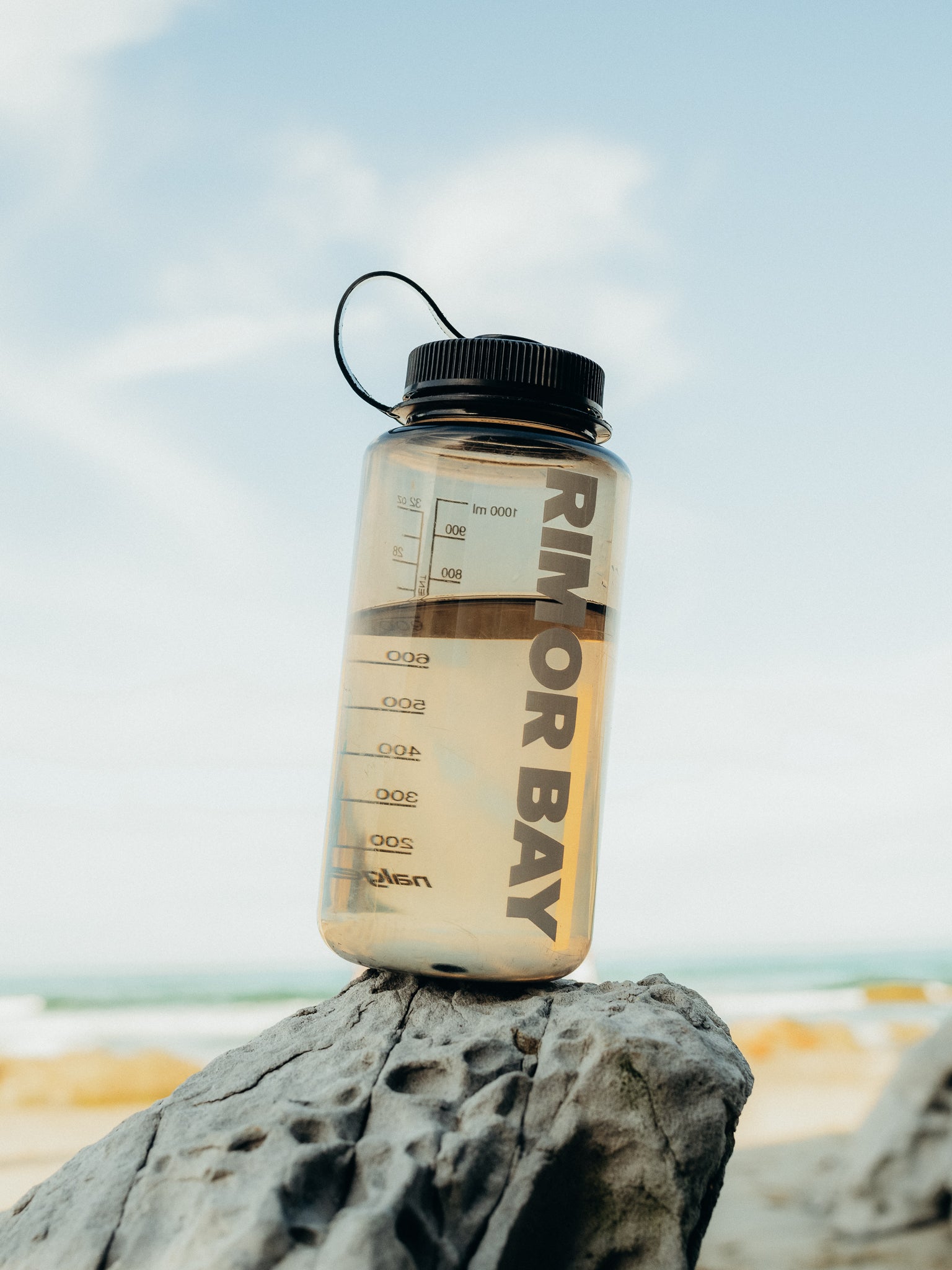brown tinted water bottle with logo on a rock at the beach